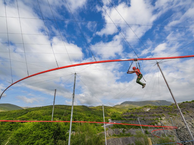 A man flying on a zipping adventure with mountains and a blue sky in the background