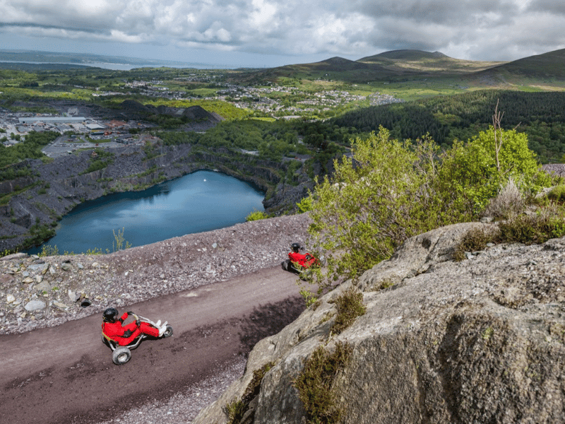 Two people karting on a mountain track with a lake below